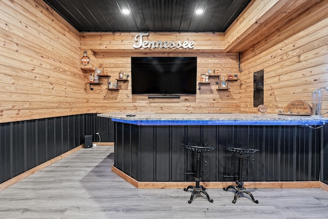 bar with light wood-type flooring and wood walls