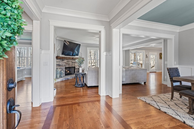 interior space with ornamental molding, ceiling fan, a stone fireplace, and wood-type flooring