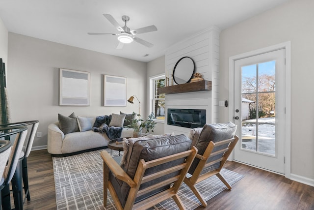 living room featuring ceiling fan, a large fireplace, and dark hardwood / wood-style floors