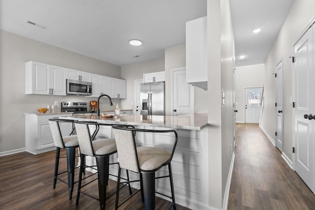 kitchen featuring sink, light stone countertops, a breakfast bar area, stainless steel appliances, and white cabinets