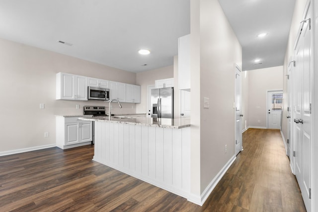 kitchen featuring light stone countertops, white cabinets, appliances with stainless steel finishes, and dark hardwood / wood-style flooring