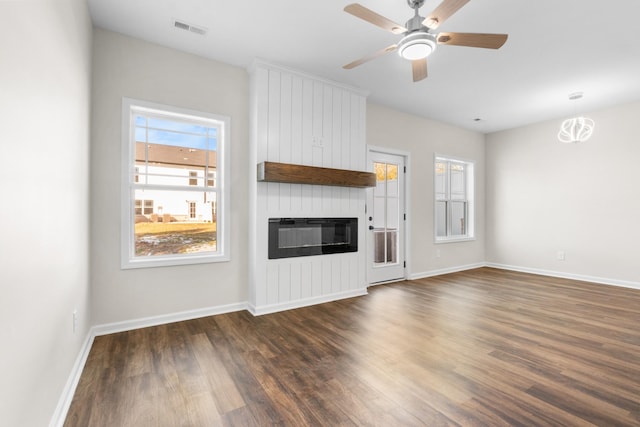 unfurnished living room featuring dark wood-type flooring, a large fireplace, a healthy amount of sunlight, and ceiling fan