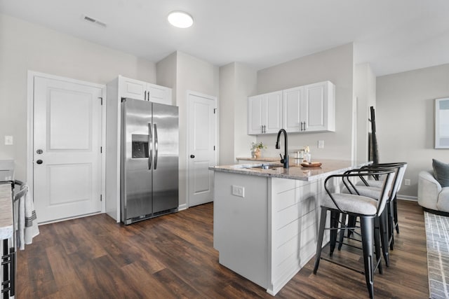 kitchen with white cabinets, stainless steel refrigerator with ice dispenser, sink, kitchen peninsula, and a breakfast bar area