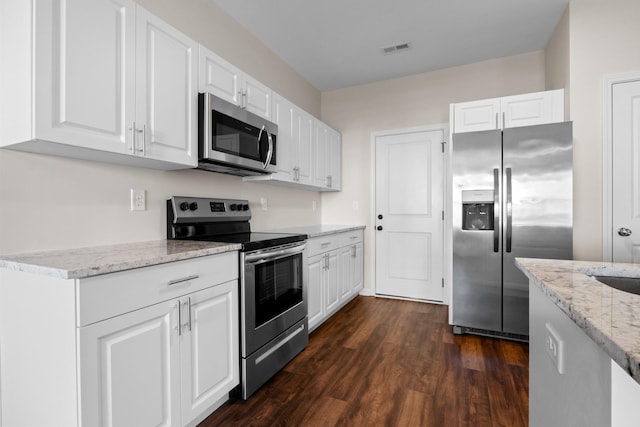 kitchen with light stone countertops, white cabinets, appliances with stainless steel finishes, and dark hardwood / wood-style floors