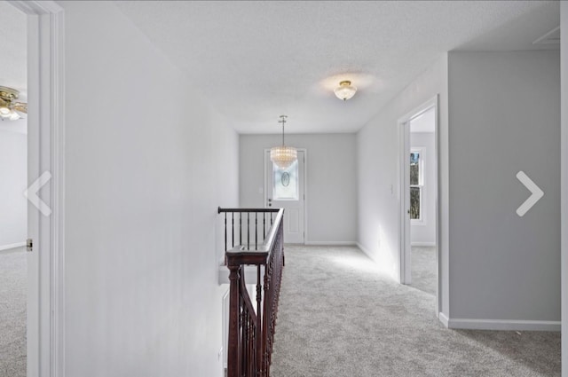 corridor with carpet flooring, a textured ceiling, and a chandelier