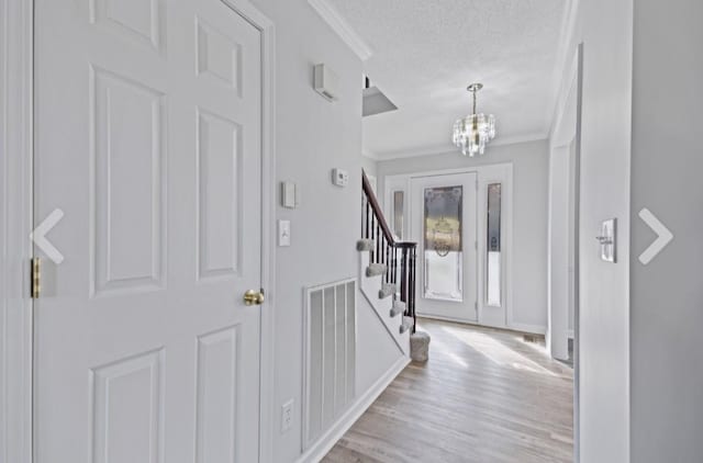 entrance foyer featuring a notable chandelier, light hardwood / wood-style flooring, crown molding, and a textured ceiling