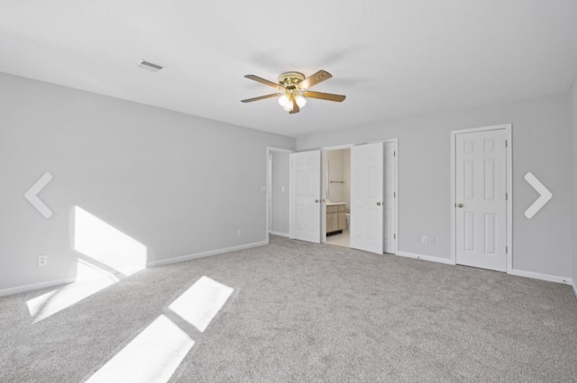 unfurnished bedroom featuring light colored carpet, ceiling fan, multiple closets, and connected bathroom