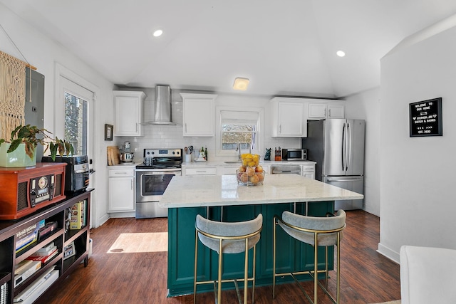 kitchen with vaulted ceiling, stainless steel appliances, white cabinets, wall chimney range hood, and backsplash