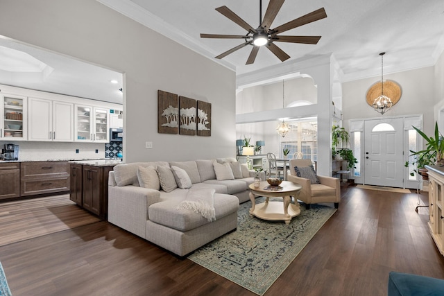 living room with ceiling fan with notable chandelier, a high ceiling, ornamental molding, and dark hardwood / wood-style floors