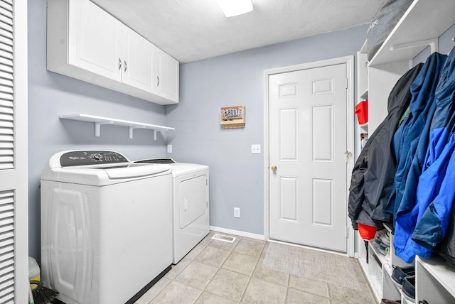 clothes washing area with washing machine and clothes dryer, light tile patterned floors, and cabinets