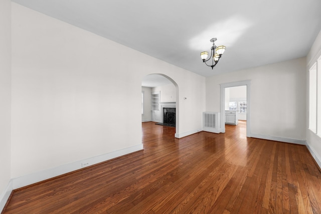 spare room with a notable chandelier, dark wood-type flooring, built in features, and a premium fireplace