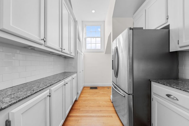 kitchen featuring tasteful backsplash, light hardwood / wood-style flooring, dark stone countertops, stainless steel fridge, and white cabinets