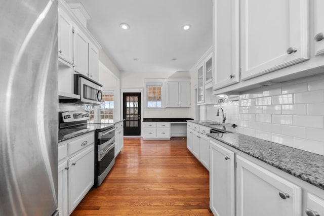 kitchen with hardwood / wood-style floors, white cabinetry, sink, stainless steel appliances, and light stone countertops