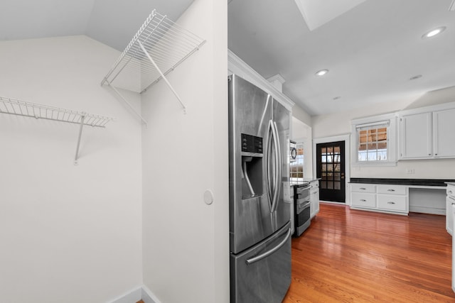 kitchen with appliances with stainless steel finishes, built in desk, white cabinetry, lofted ceiling, and hardwood / wood-style flooring