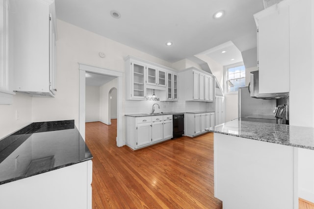 kitchen with white cabinetry, dark stone countertops, black dishwasher, kitchen peninsula, and light hardwood / wood-style floors