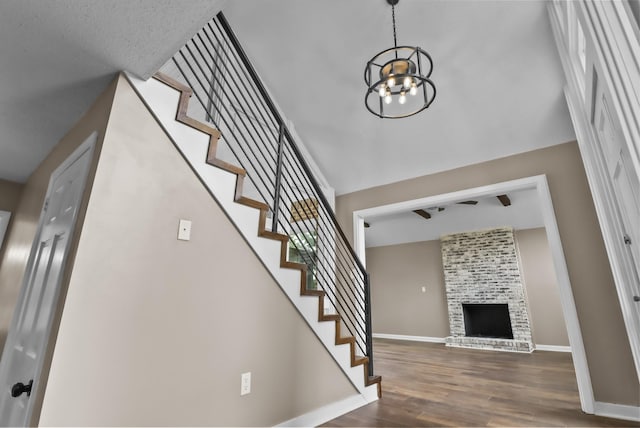 staircase featuring a brick fireplace, an inviting chandelier, and hardwood / wood-style floors