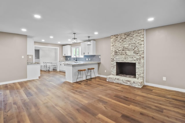 kitchen featuring hanging light fixtures, kitchen peninsula, a breakfast bar, a brick fireplace, and white cabinetry