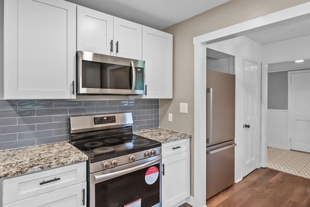 kitchen with stainless steel appliances, dark hardwood / wood-style flooring, light stone counters, white cabinets, and tasteful backsplash