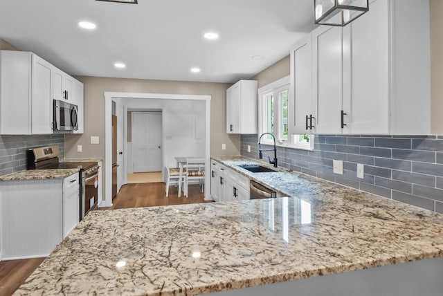 kitchen with stainless steel appliances, white cabinetry, sink, and light stone counters