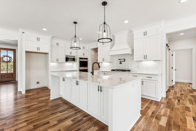 kitchen featuring stainless steel appliances, custom exhaust hood, a kitchen island with sink, and white cabinets