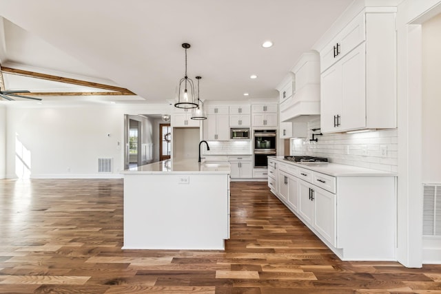 kitchen with appliances with stainless steel finishes, an island with sink, pendant lighting, white cabinets, and tasteful backsplash