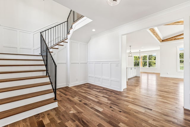 stairs with vaulted ceiling, a chandelier, ornamental molding, and wood-type flooring