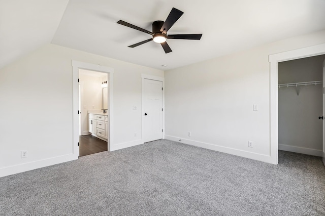 unfurnished bedroom with ceiling fan, ensuite bathroom, vaulted ceiling, and dark colored carpet