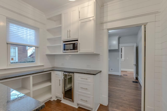 kitchen featuring stainless steel microwave, dark wood-type flooring, beverage cooler, white cabinetry, and dark stone countertops