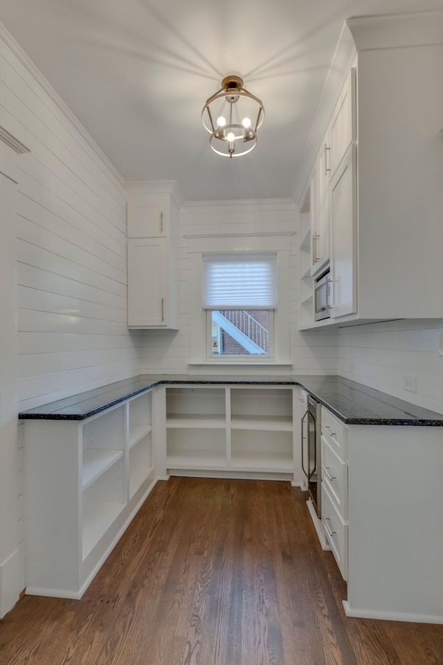 kitchen featuring dark stone counters, dark wood-type flooring, stainless steel microwave, white cabinets, and an inviting chandelier