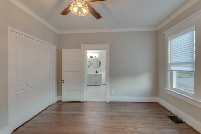 unfurnished bedroom with a closet, connected bathroom, crown molding, dark hardwood / wood-style flooring, and ceiling fan