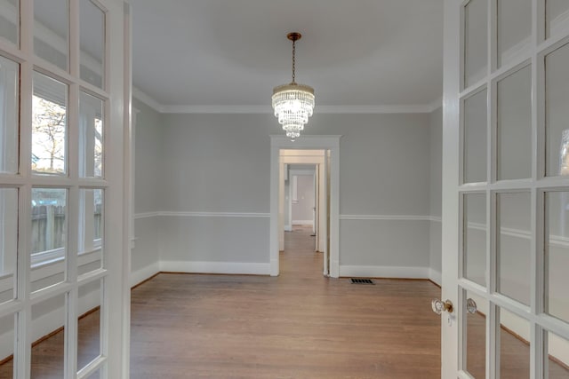 unfurnished dining area with a notable chandelier, crown molding, and light hardwood / wood-style floors