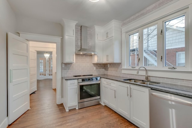 kitchen featuring sink, white cabinets, wall chimney exhaust hood, dark stone countertops, and appliances with stainless steel finishes