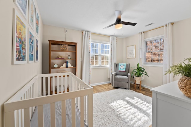 bedroom with ceiling fan, light wood-type flooring, and a crib