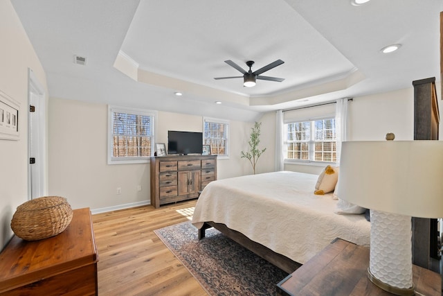 bedroom with ceiling fan, a tray ceiling, and light hardwood / wood-style flooring