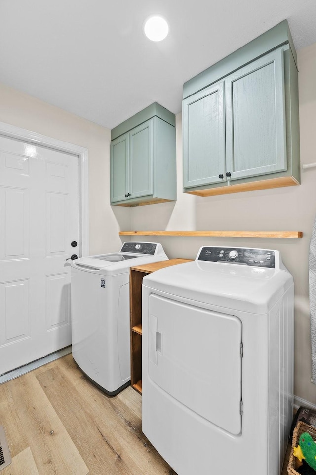 laundry area with light wood-type flooring, cabinets, and separate washer and dryer