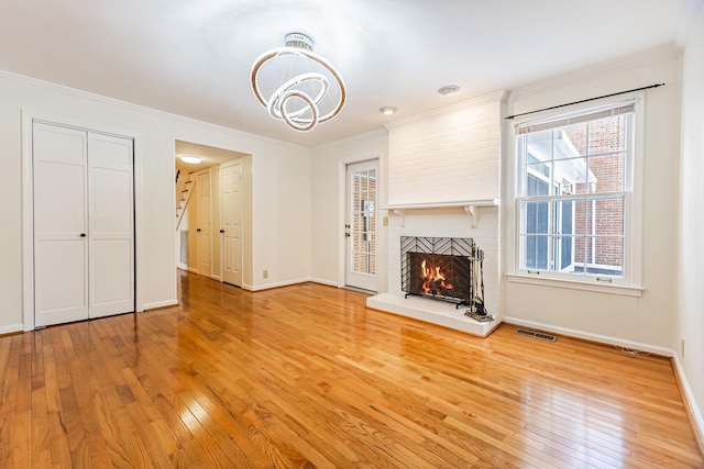 unfurnished living room with a brick fireplace, a notable chandelier, hardwood / wood-style flooring, and crown molding