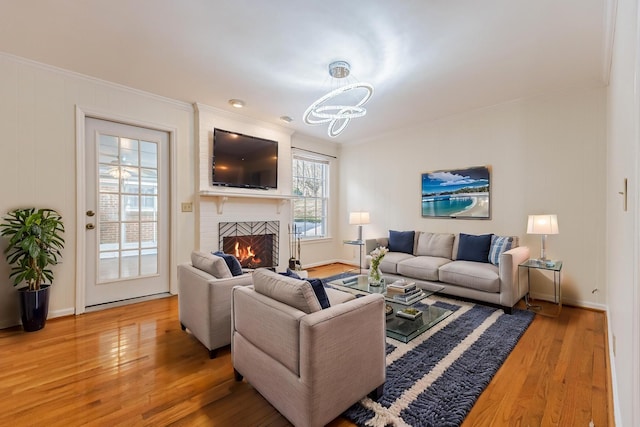 living room with a brick fireplace, crown molding, a chandelier, and hardwood / wood-style flooring