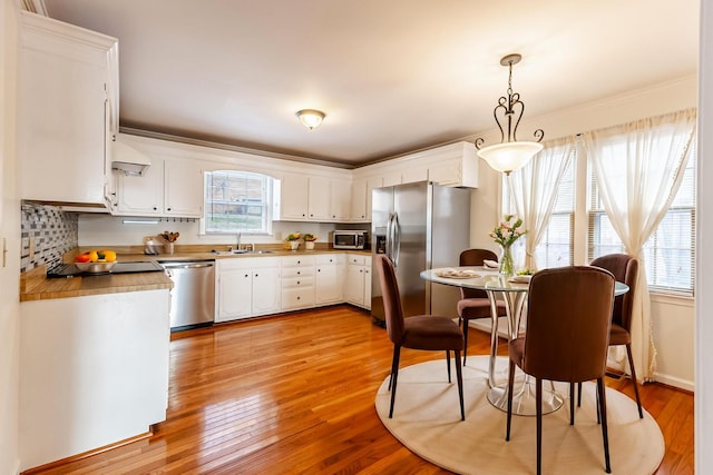 kitchen featuring pendant lighting, light hardwood / wood-style floors, white cabinetry, appliances with stainless steel finishes, and sink