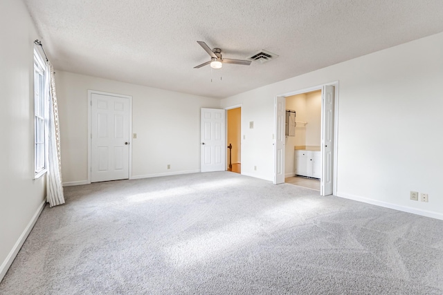 unfurnished bedroom featuring ceiling fan, ensuite bathroom, light carpet, and a textured ceiling