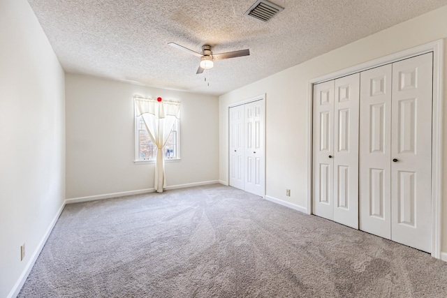 unfurnished bedroom featuring carpet flooring, two closets, ceiling fan, and a textured ceiling