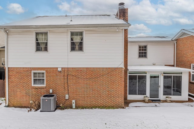 snow covered back of property featuring central air condition unit and a sunroom