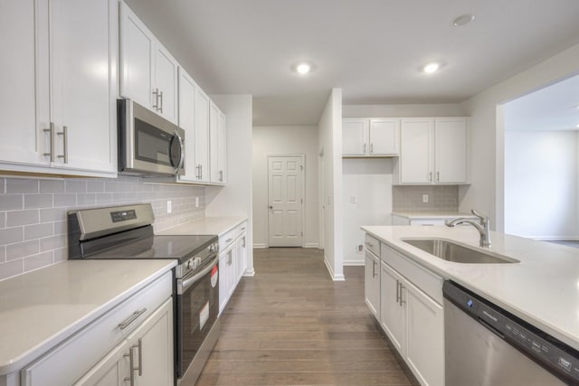 kitchen featuring tasteful backsplash, hardwood / wood-style floors, white cabinets, appliances with stainless steel finishes, and sink