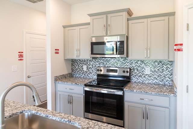 kitchen featuring stainless steel appliances, tasteful backsplash, a sink, and light stone countertops