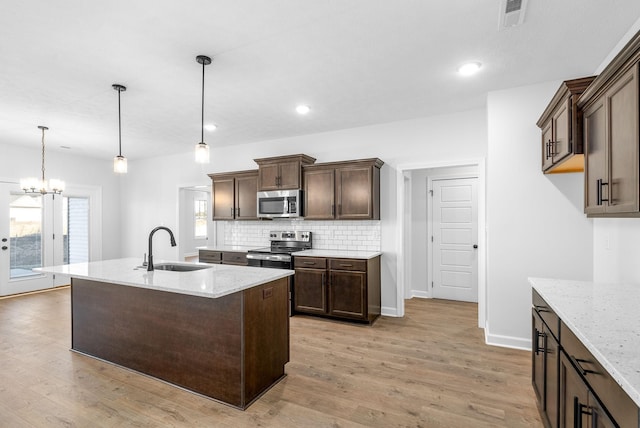 kitchen with sink, light wood-type flooring, pendant lighting, stainless steel appliances, and light stone countertops