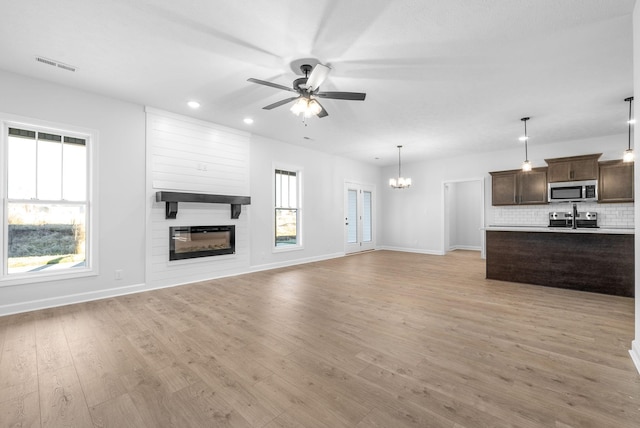 unfurnished living room featuring ceiling fan with notable chandelier, a fireplace, and light hardwood / wood-style floors