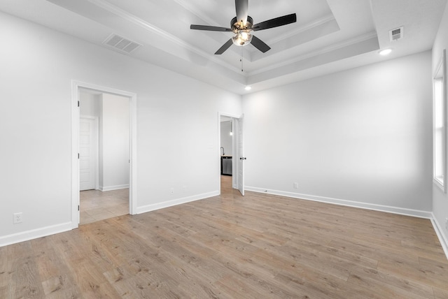 spare room with a tray ceiling, ornamental molding, ceiling fan, and light wood-type flooring