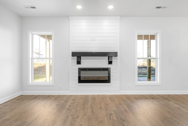 unfurnished living room with hardwood / wood-style flooring, a large fireplace, and a wealth of natural light