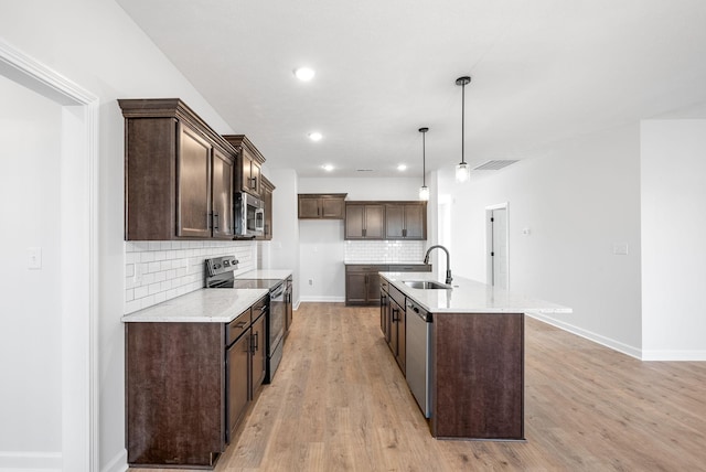 kitchen featuring appliances with stainless steel finishes, pendant lighting, sink, a kitchen island with sink, and light hardwood / wood-style floors