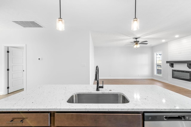 kitchen with decorative light fixtures, dishwasher, sink, a large fireplace, and light stone counters