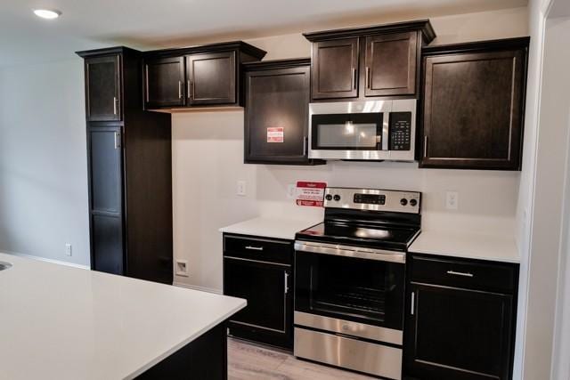 kitchen featuring stainless steel appliances, light countertops, light wood-style floors, and dark brown cabinetry